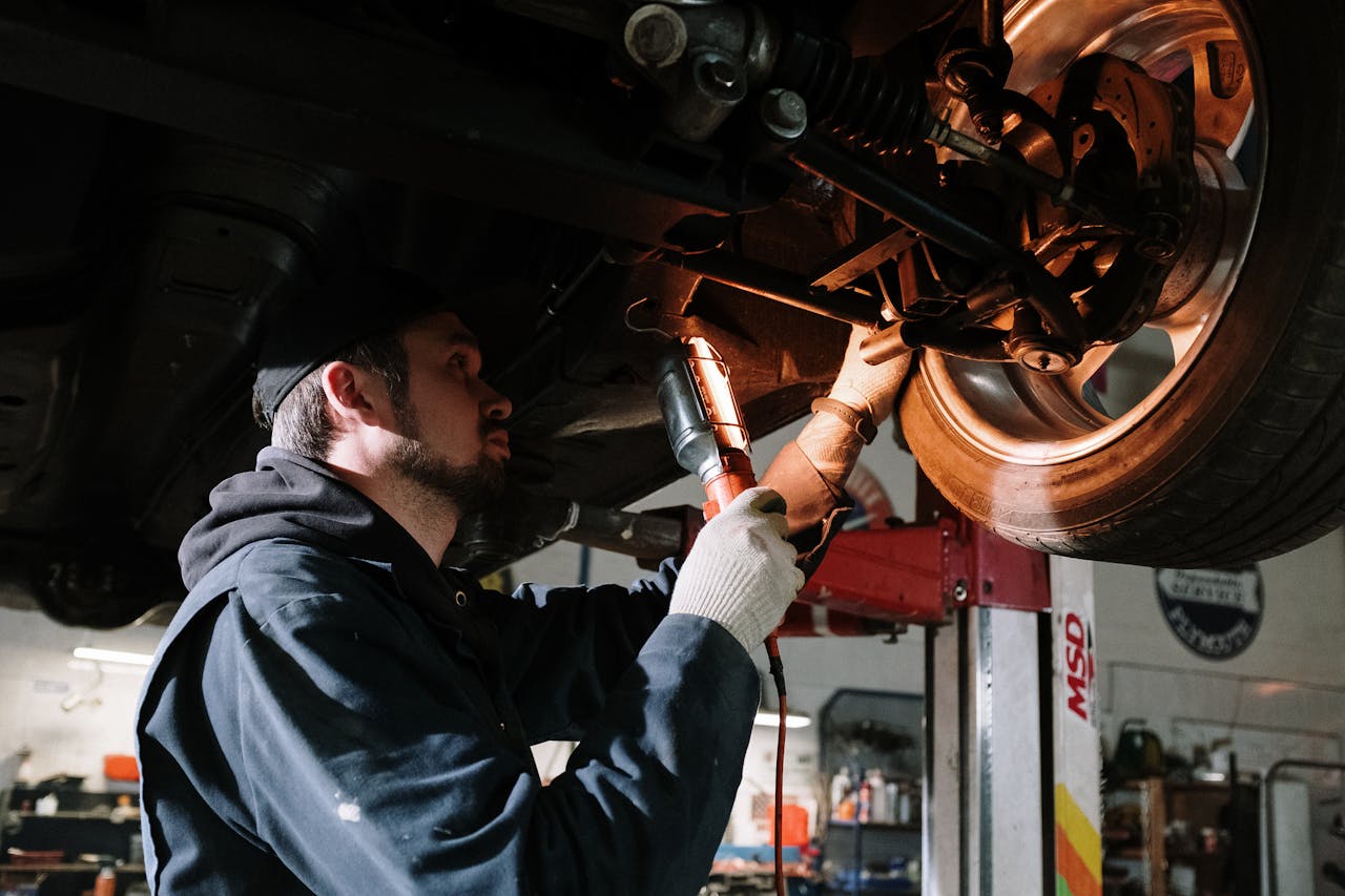 services-01 Mechanic examining car's undercarriage at a garage, focusing on vehicle maintenance.