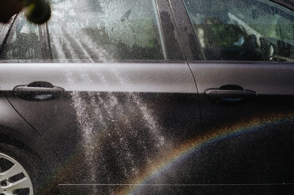 pexels photo 4870671 Close-up of a car being washed with a visible rainbow in sunlight.