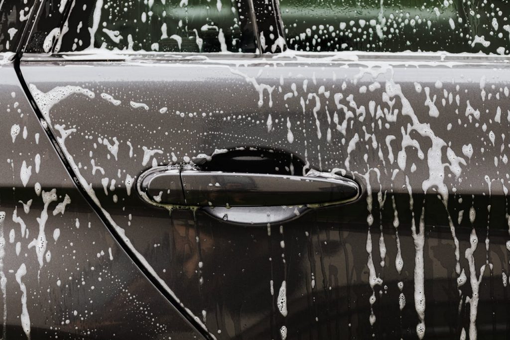 pexels photo 4870724 Detailed close-up of soap suds on a black car door during a wash, highlighting automotive care.