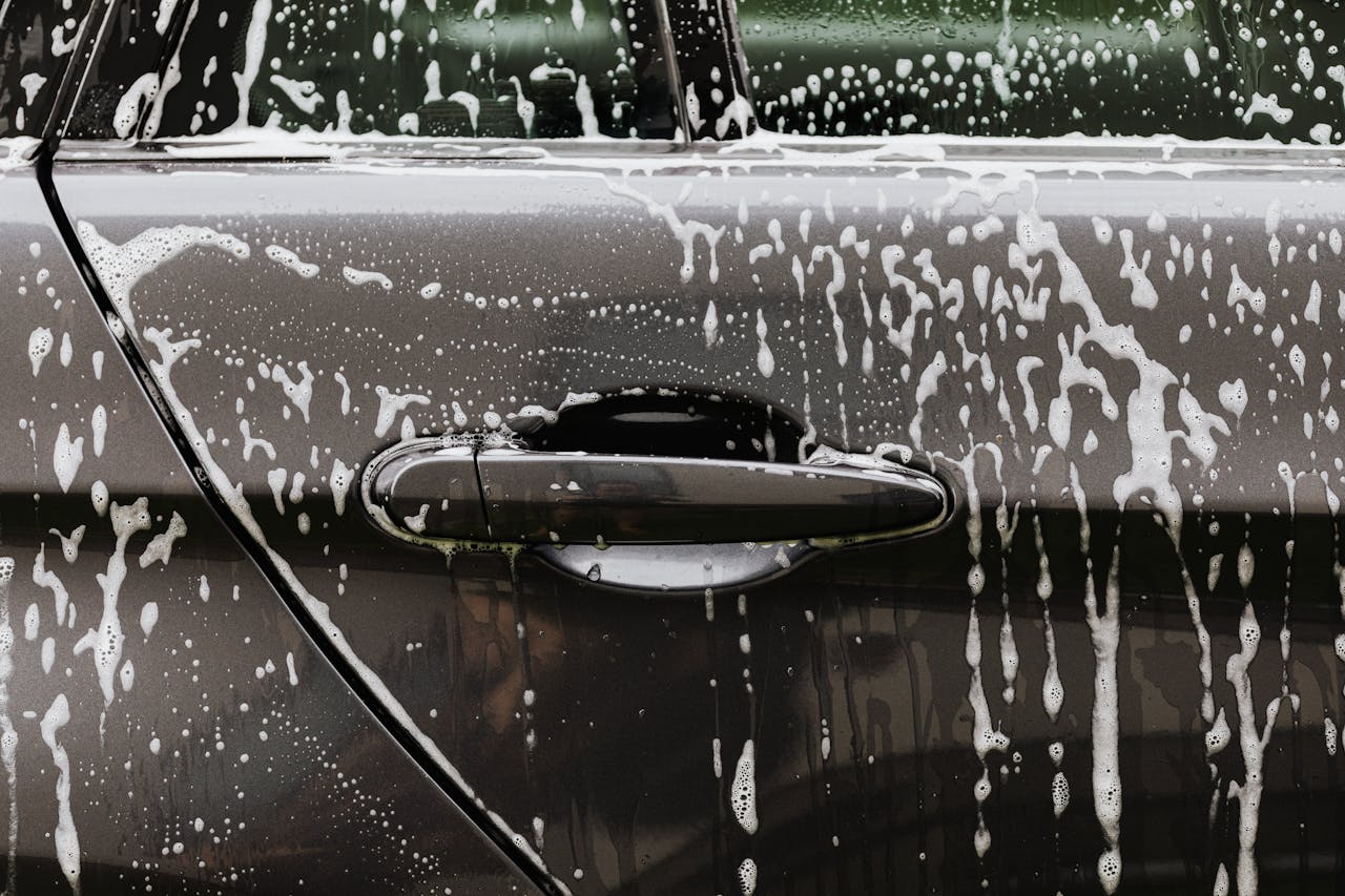 Detailed close-up of soap suds on a black car door during a wash, highlighting automotive care.