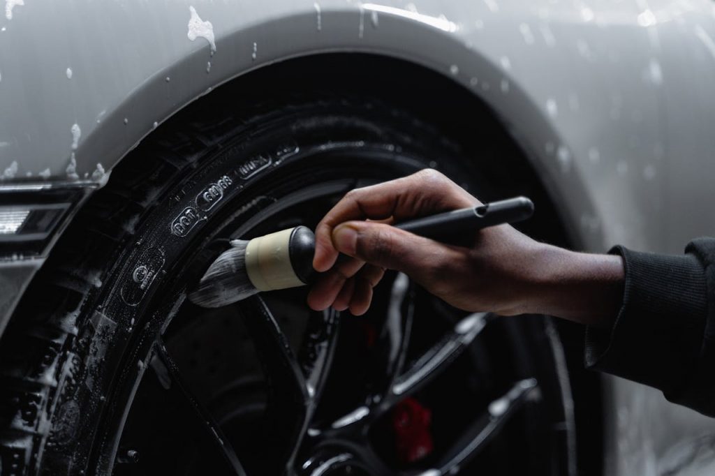 pexels photo 6872147 Detailed shot of a hand using a brush to clean a car tire and wheel during a wash.