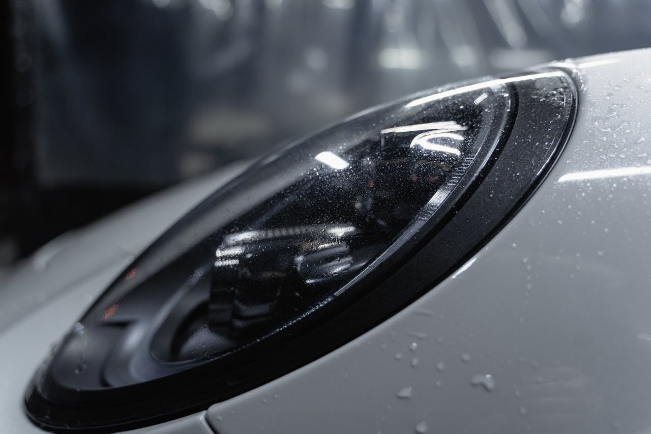 about-us-02 Detailed shot of a sleek car headlight with water droplets enhancing its glossy surface.