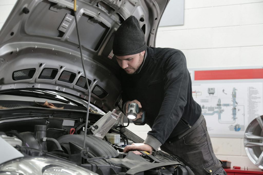 pexels photo 3807277 3807277 A mechanic closely inspects a car engine in a garage using a flashlight, ensuring proper maintenance.